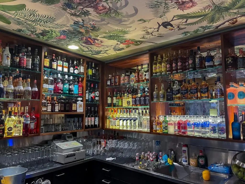 Cocktail bar at stattHotel Zurich with illuminated bottle shelves and floral ceiling